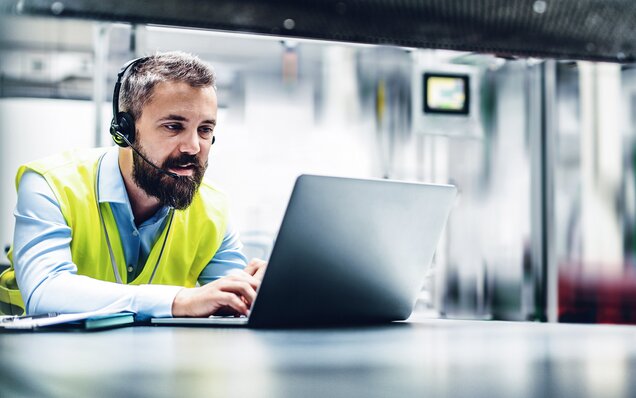 Mann arbeitet mit Laptop und Headset