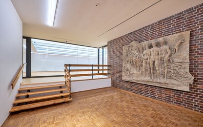 Galerie mit Holztreppe und Wandrelief