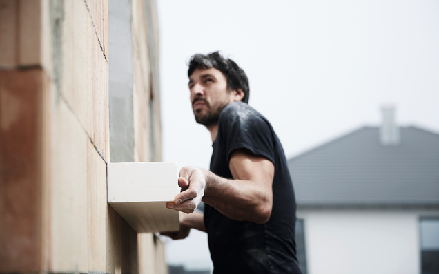 Construction worker installs GU front mounting frame on a house wall during shell construction